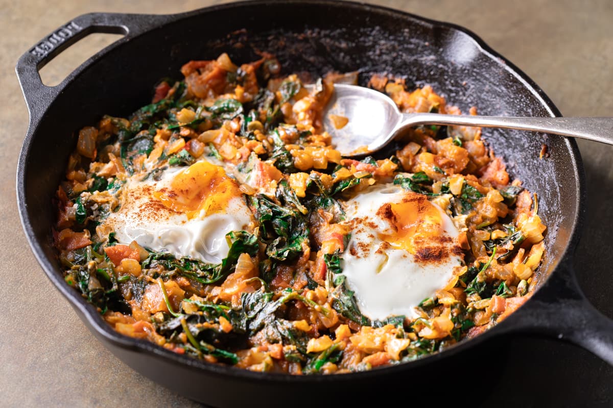 Easy shakshuka with fresh tomato and spinach cooked in a cast iron skillet