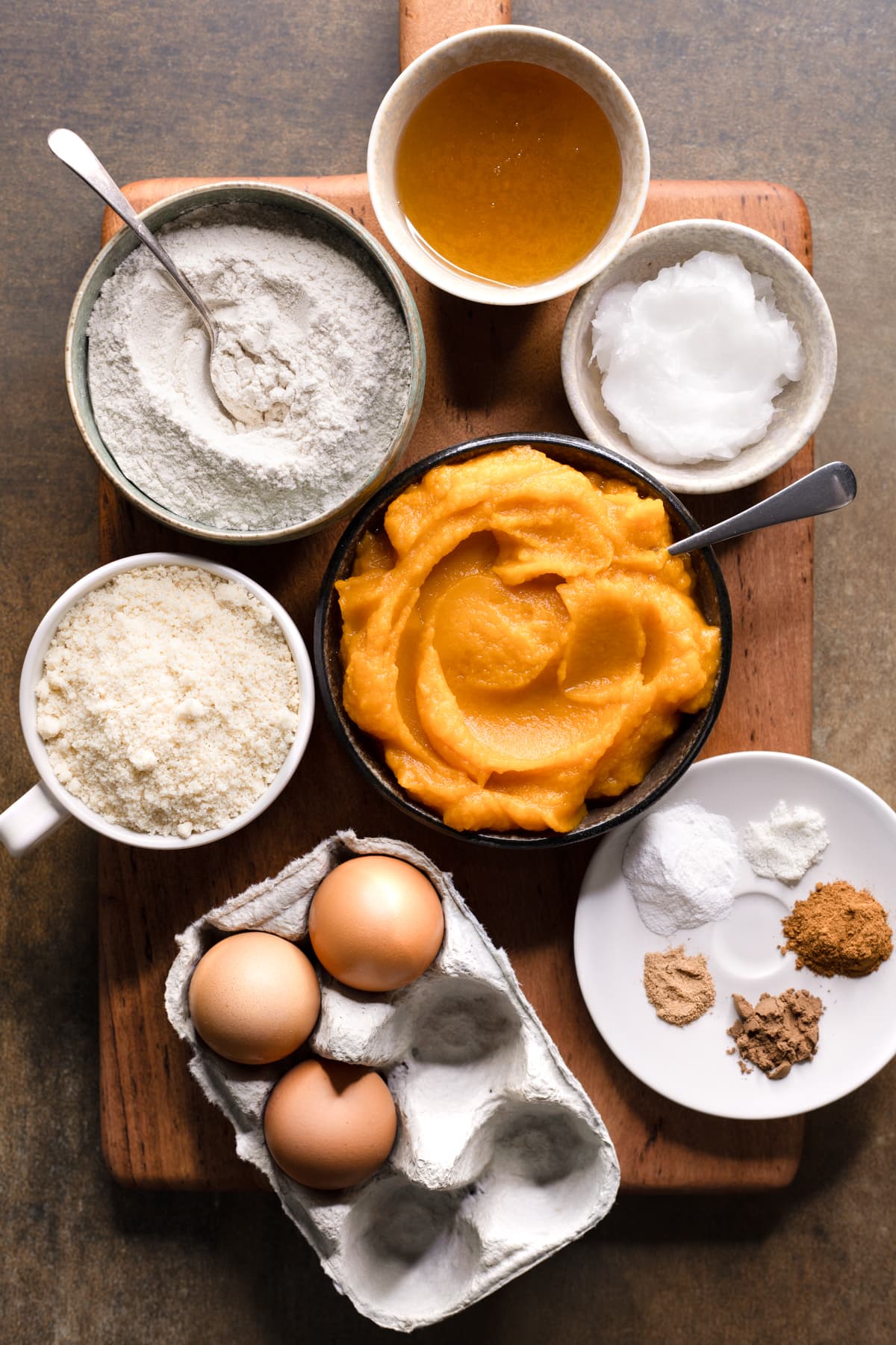 Ingredients for gluten-free pumpkin bread set out in bowls on a wooden board