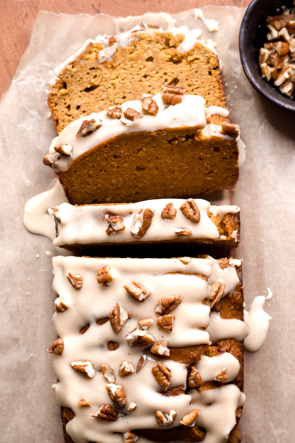 Slices of gluten-free pumpkin bread with maple glaze and pecans on a wooden board