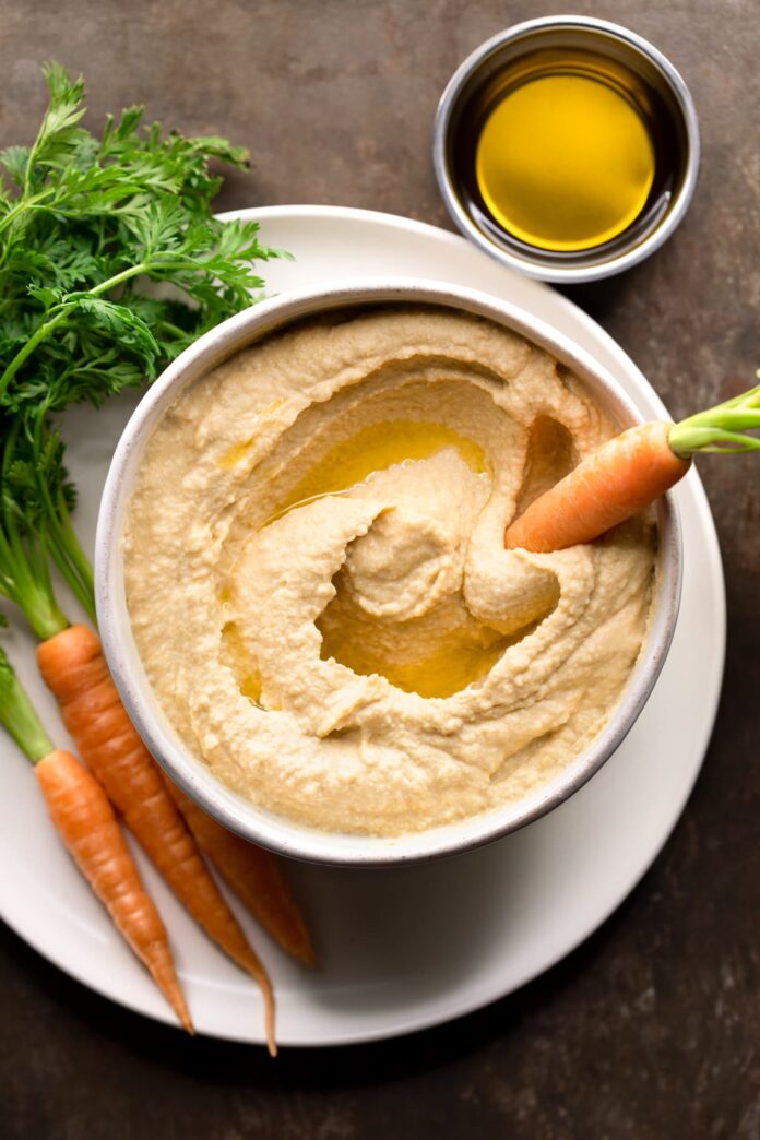 Hummus without lemon or garlic in a bowl with a raw carrot