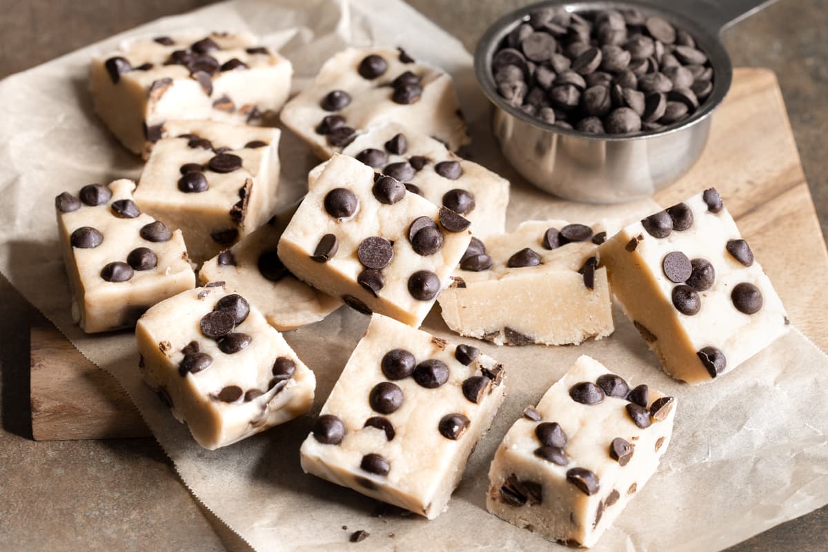 Nut-free cookie dough protein bars stacked on a sheet of baking paper with a cup of chocolate chips