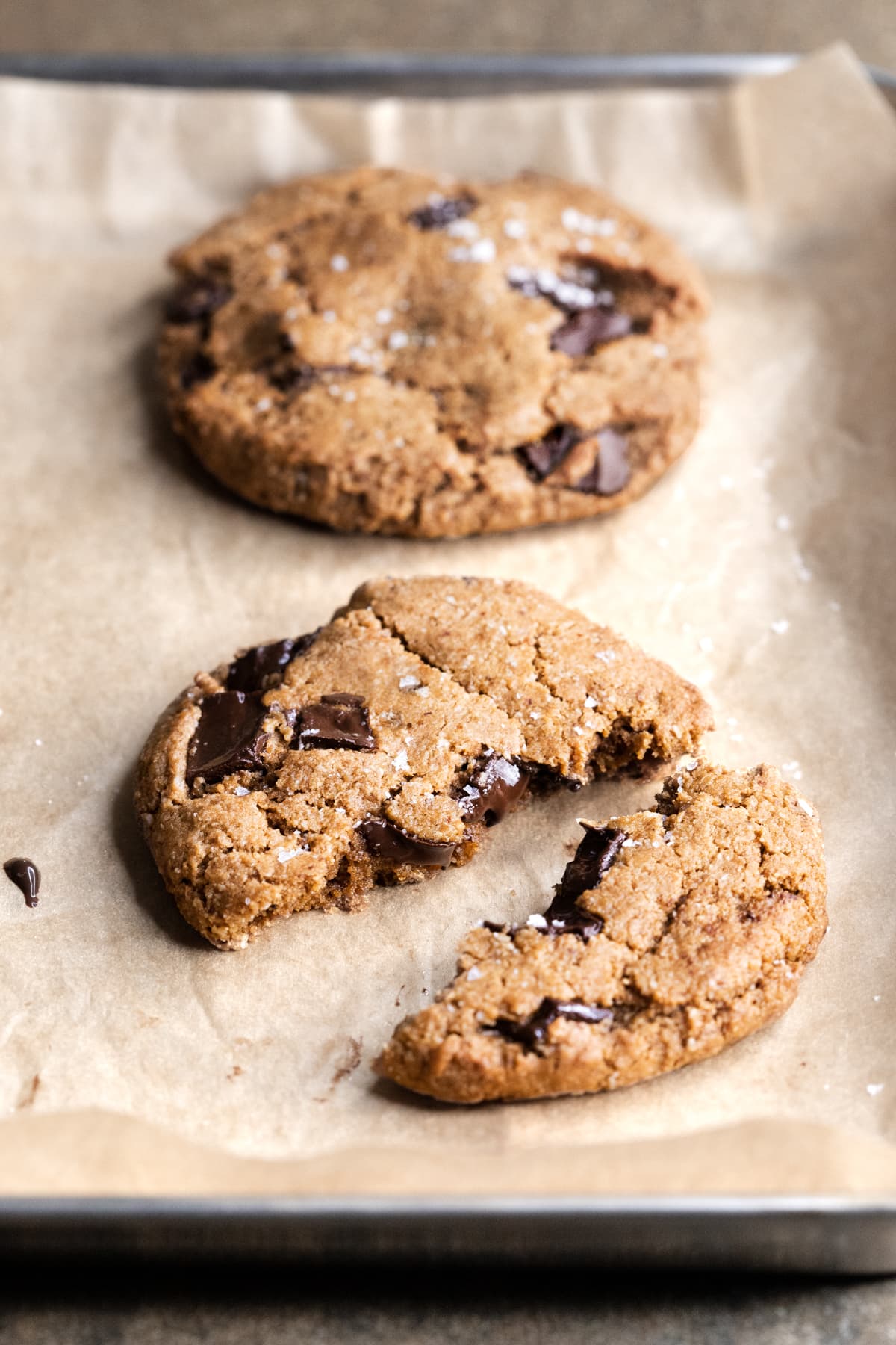 Two chocolate chip cookies on a tray with one cookie broken in half