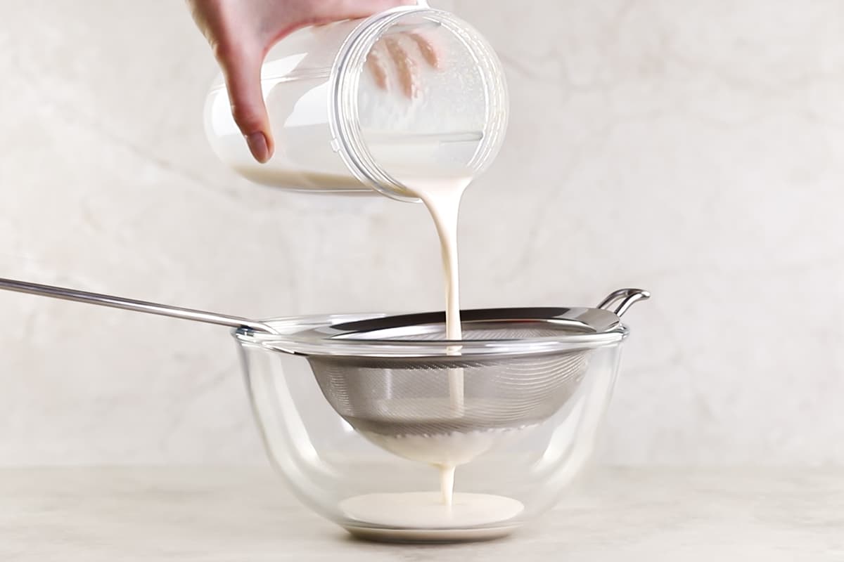 Straining oat milk through a sieve into a bowl